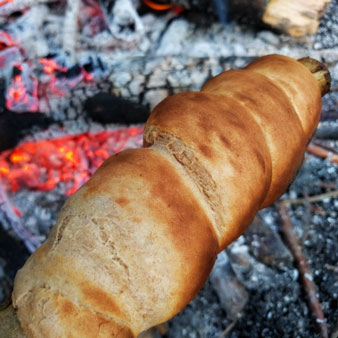 Schlangenbrot am Stock über dem Feuer