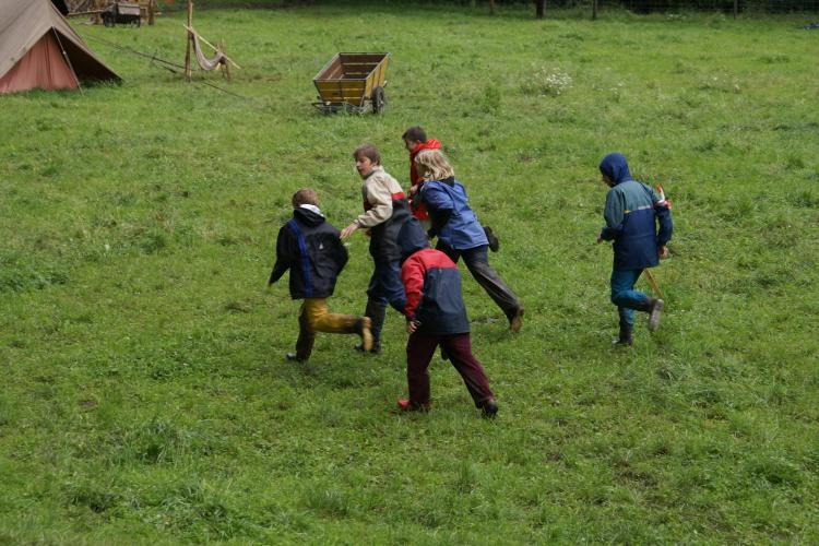 Sechs Teilnehmer*innen sind joggend unterwegs beim Spiel «Karawanenüberfall». Im Hintergrund sieht man den Zeltplatz.